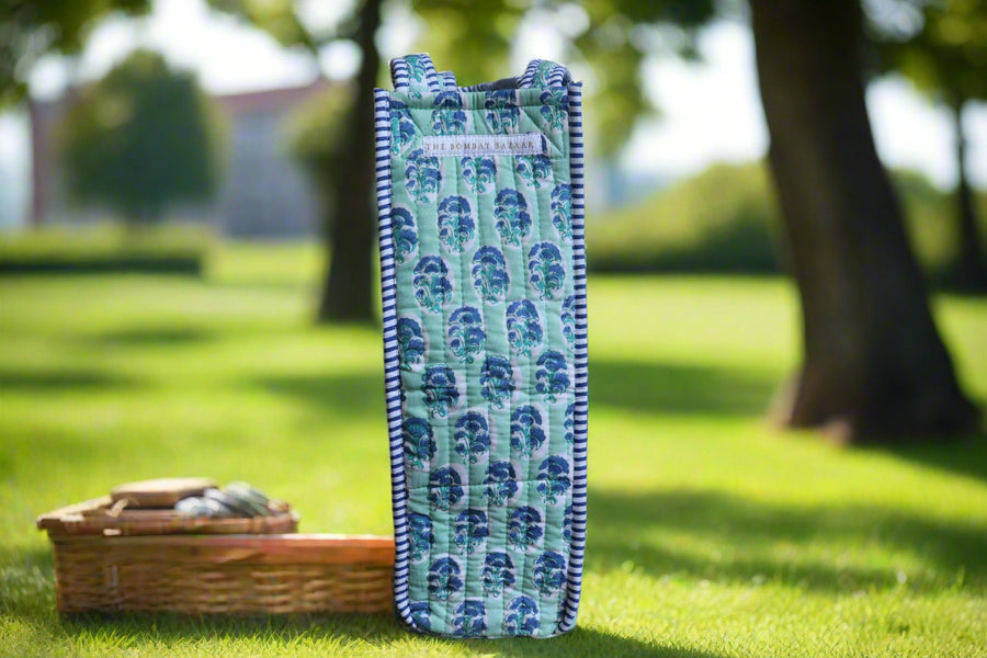 Green fabric bag with blue patterns on a stone surface in front of a fireplace.