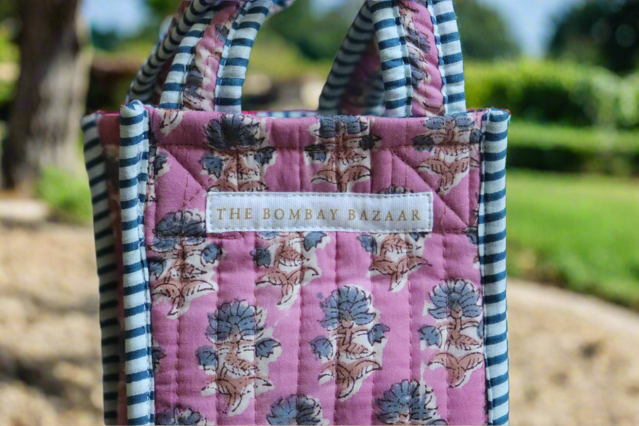 Pink quilted bag with floral patterns and striped handles, featuring 'The Bombay Bazaar' label.